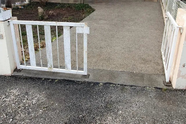 Allée gravillonnée propre, derrière un portillon blanc entrouvert
