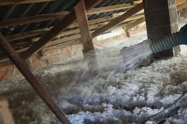 Charpente en bois vue depuis les combles, poteaux et chevrons au-dessus d'une couche d'isolant soufflé