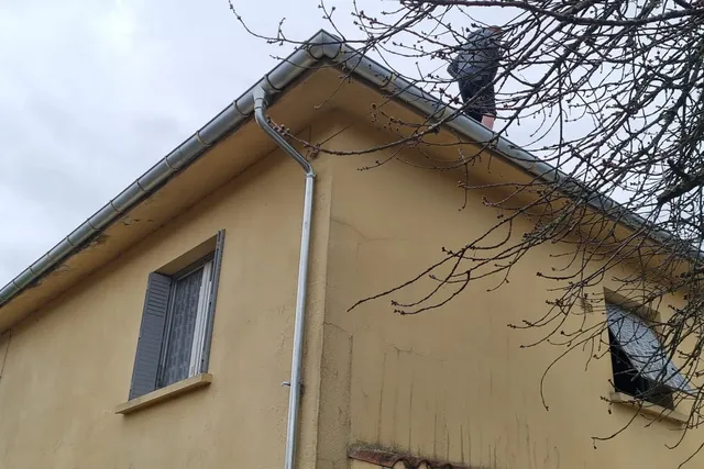 Gouttière et descente d'eau grises à l'angle d'une maison à la façade jaune