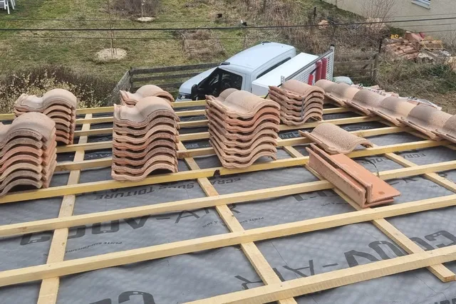 Liteaux neufs posés sur un écran sous-toiture, avec des piles de tuiles prêtes à être posées