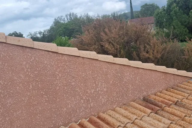 Mur pignon en crépi rose et ses tuiles de rive, en bordure d'une toiture aux tuiles propres
